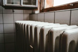 White radiator heated by a hot-water boiler beside a wooden window